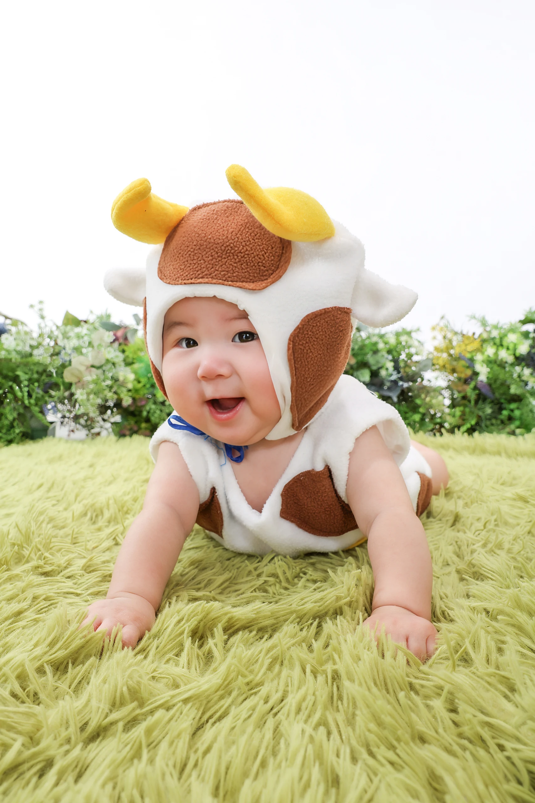牛の衣装を着て緑のラグの上で笑う赤ちゃん