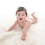 A baby happily crawling and laughing on a white rug