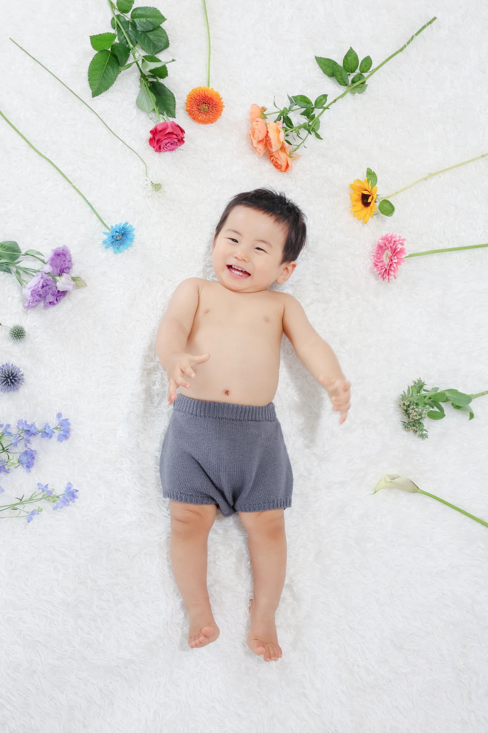 色とりどりの花に囲まれて寝転ぶ一歳児