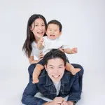 A family, with a mother and child overlapping on the father's back, laughing.