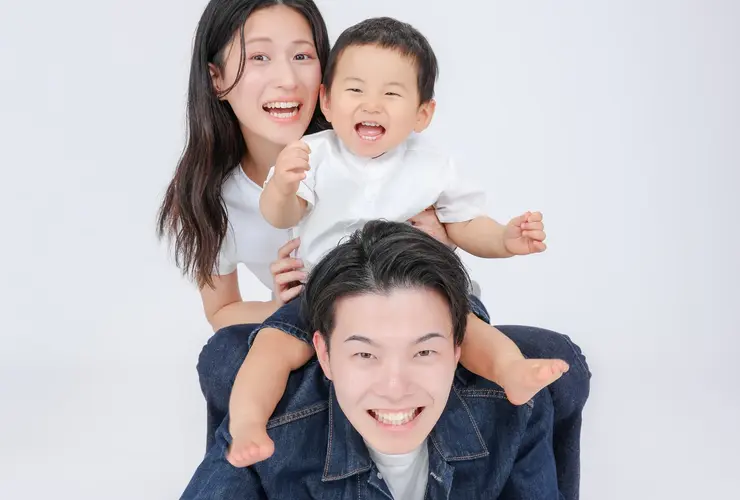 A family, with a mother and child overlapping on the father's back, laughing.
