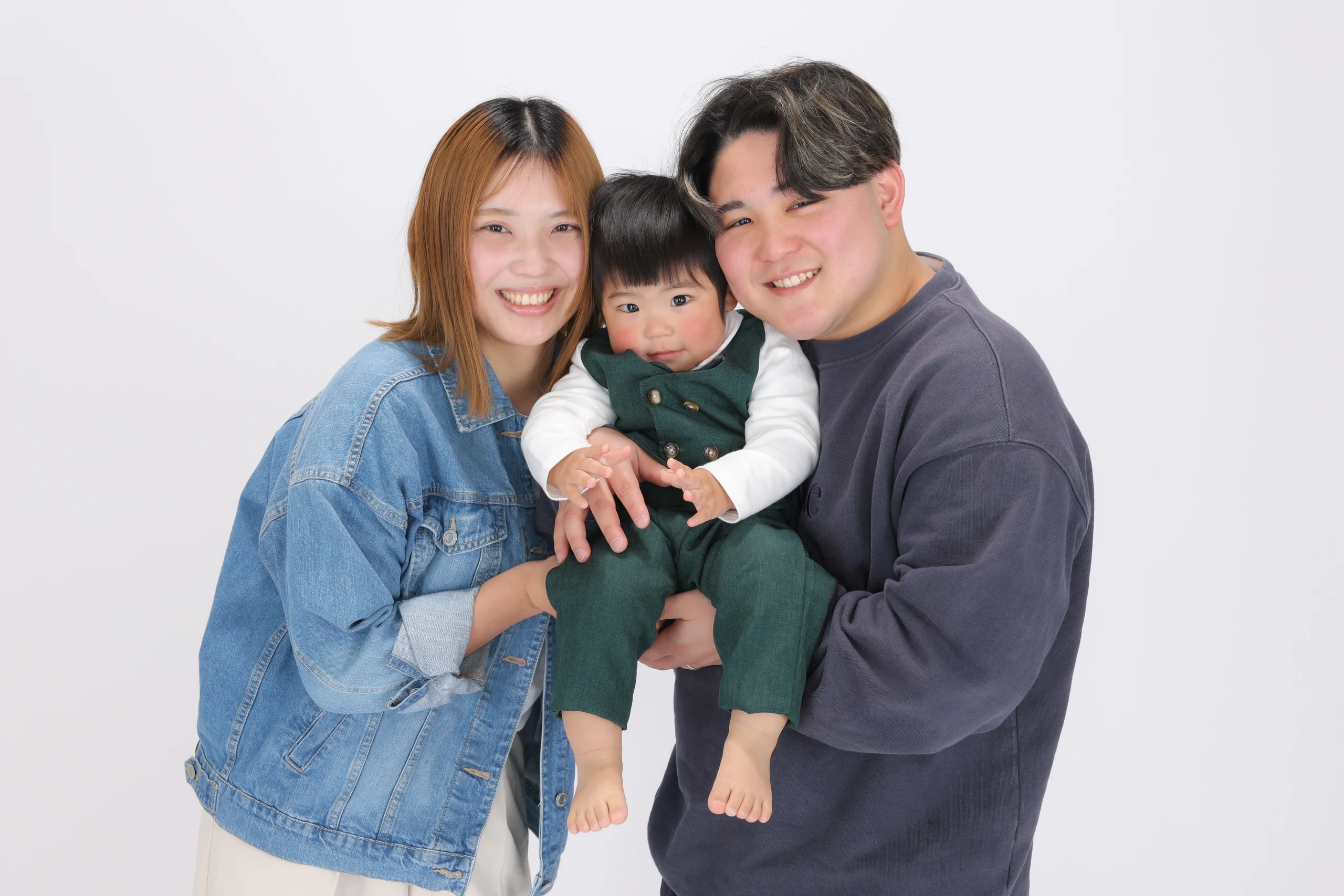 緑の衣装を着た赤ちゃんを囲んで笑う両親