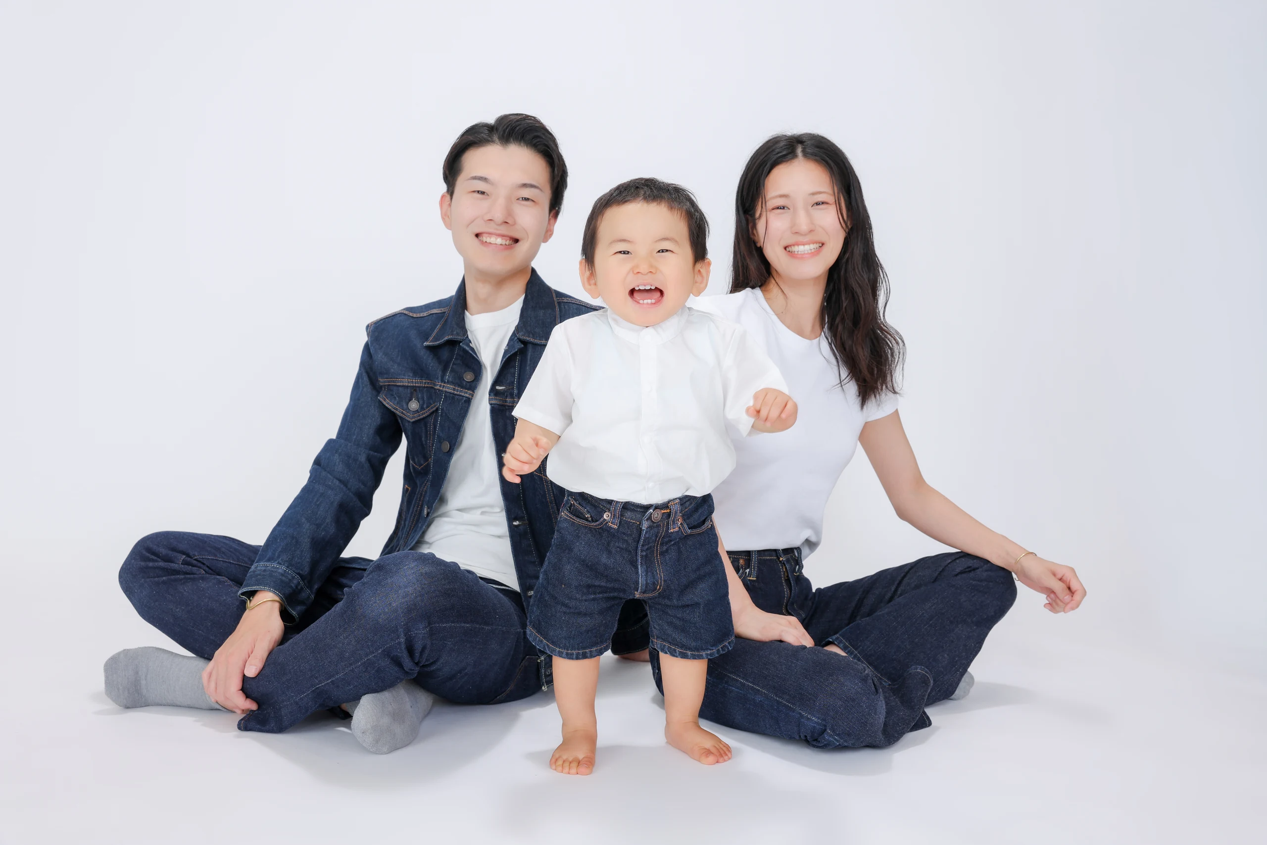 白い背景で子どもを囲んで座る両親