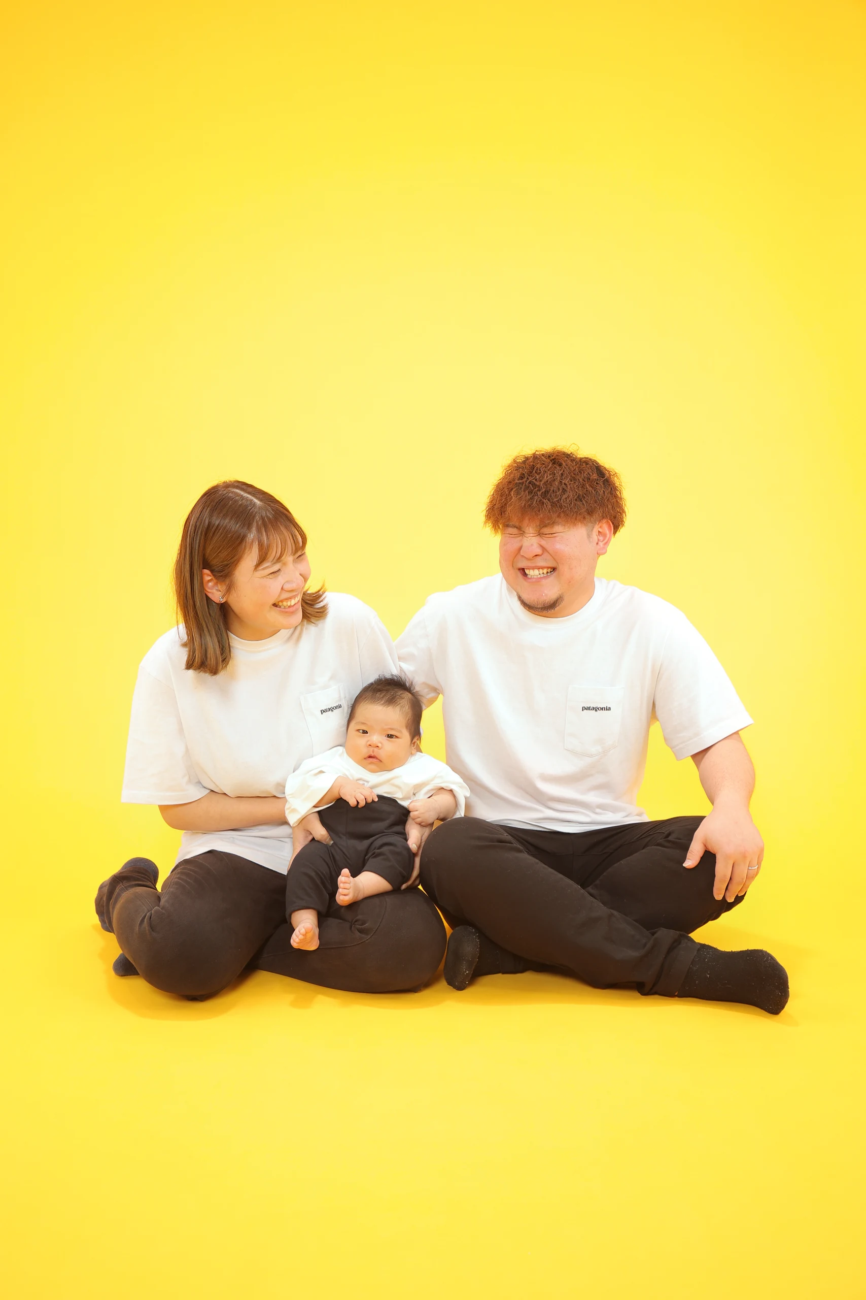 黄色い背景で赤ちゃんを囲んで座る両親