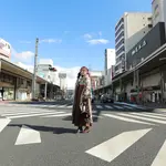 A woman in graduation hakama standing in a shopping street under a blue sky.