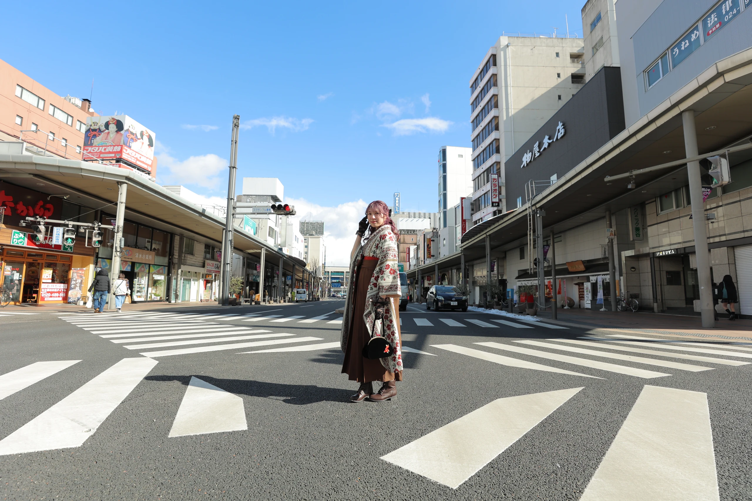 A woman in graduation hakama standing in a shopping street under a blue sky.