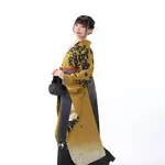 A woman in a yellow kimono and black hakama standing against a white background.