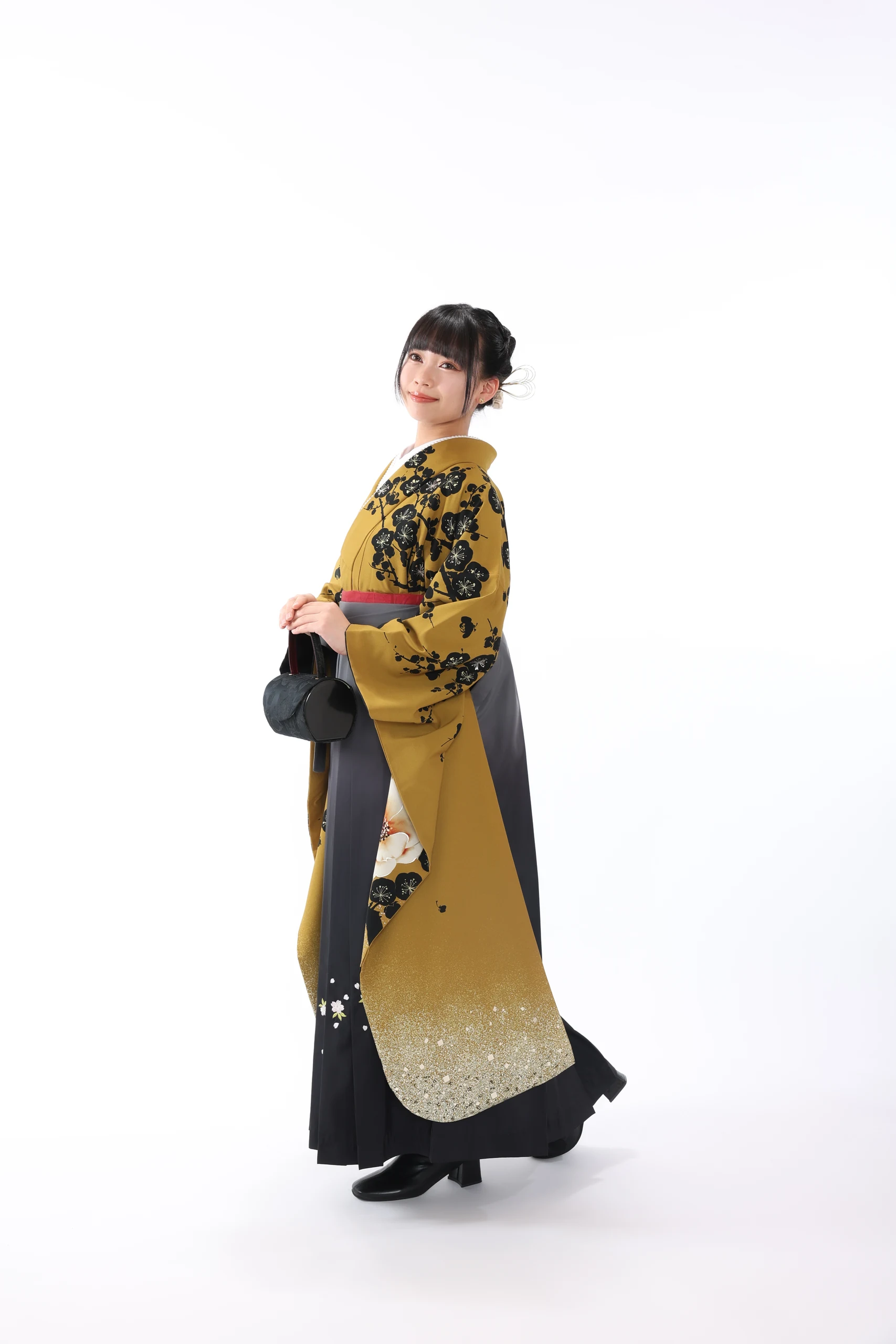 A woman in a yellow kimono and black hakama standing against a white background.