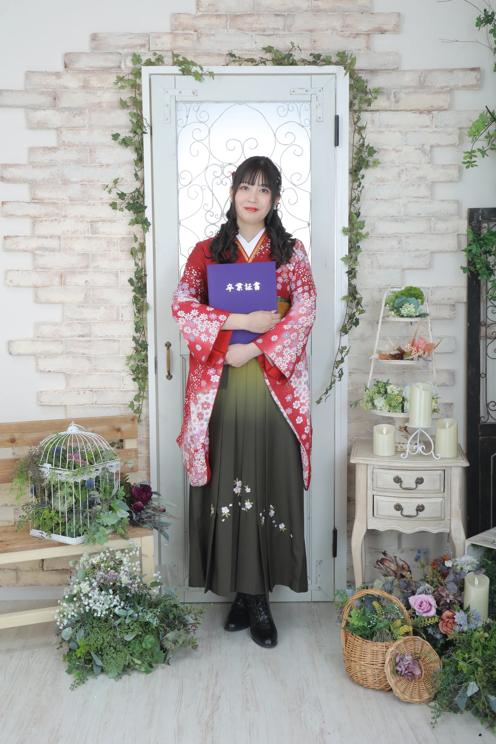 A woman in a red kimono and black hakama holding a diploma in a bright indoor set.
