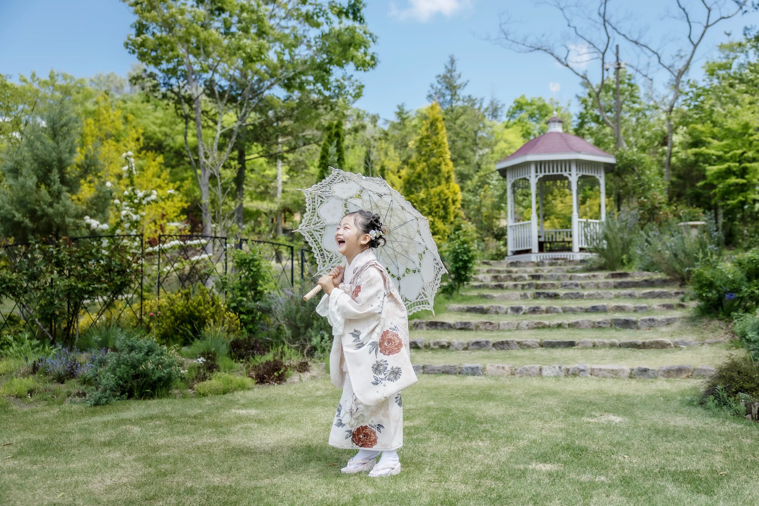 緑の庭園で白い和傘を持って笑う七五三のロケーション写真