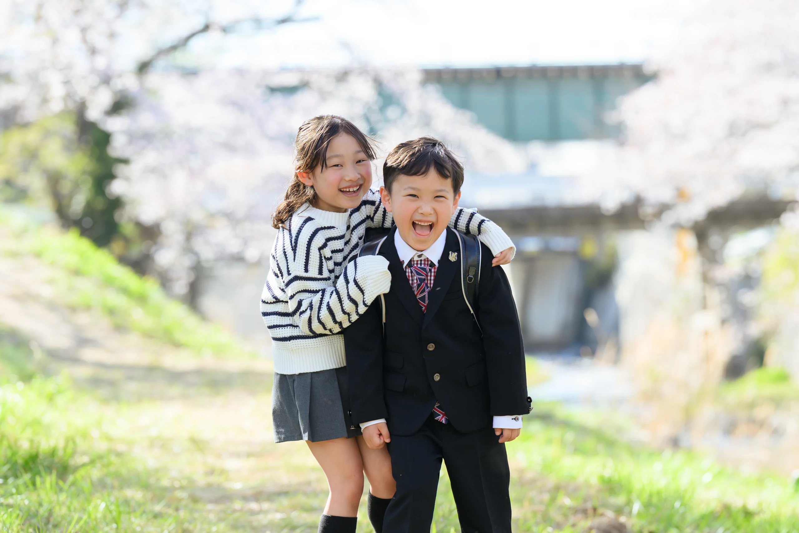 桜の下でランドセル姿の男の子と姉が笑う入学記念写真