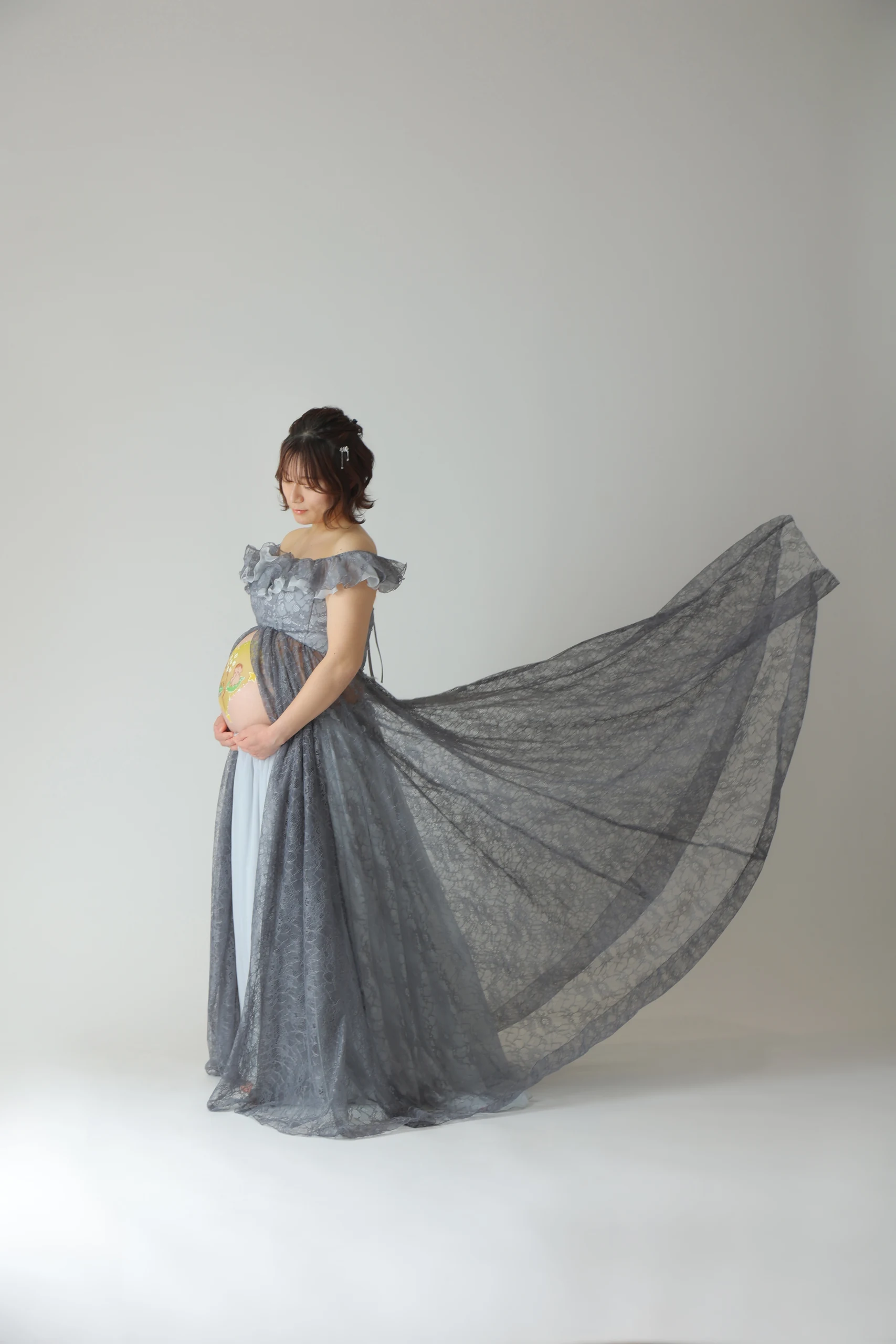 A pregnant woman standing with the hem of her gray dress flared out