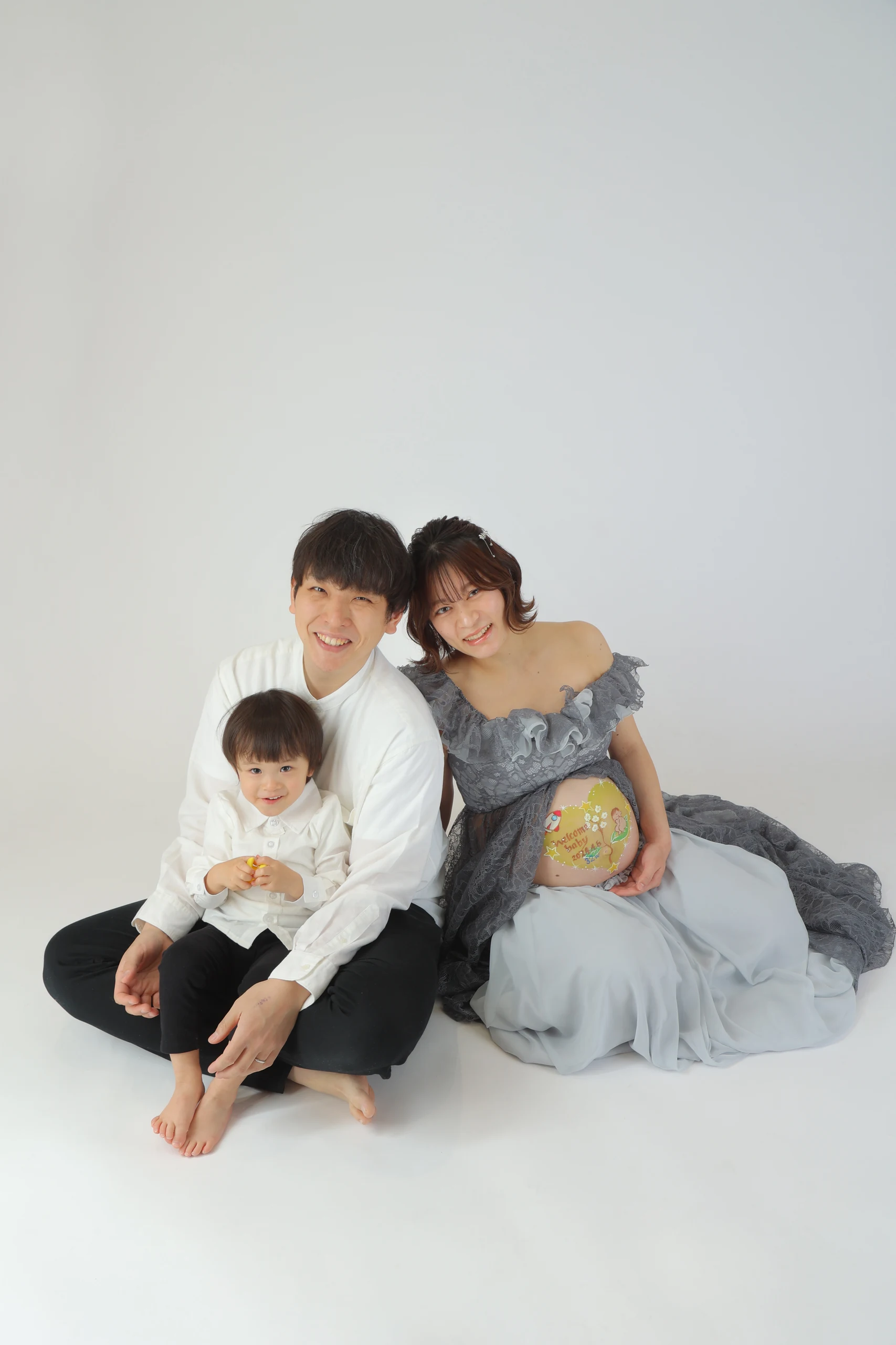A maternity couple sitting with their child against a white background