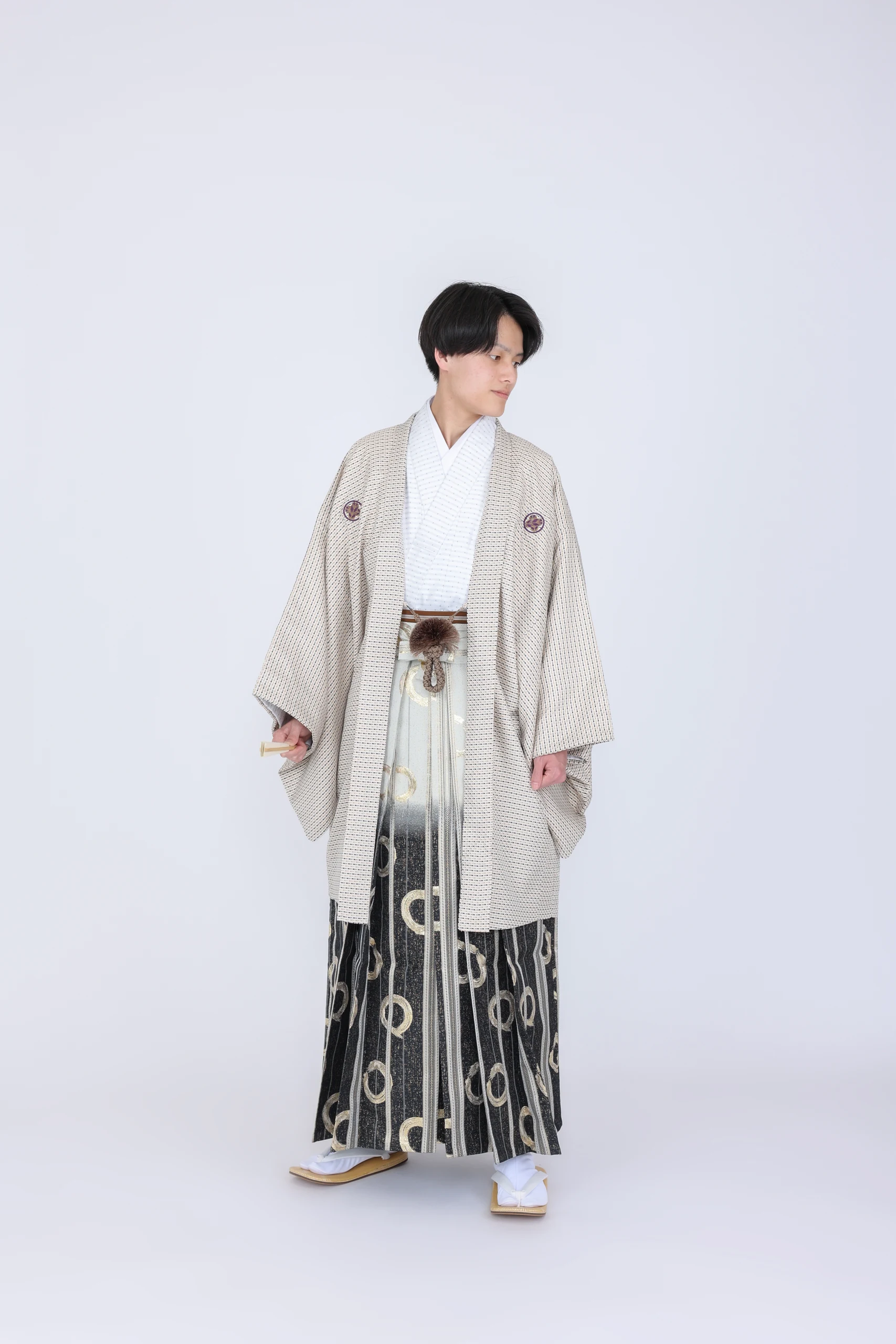 淡いベージュの紋付と黒金の袴で立つ成人男性