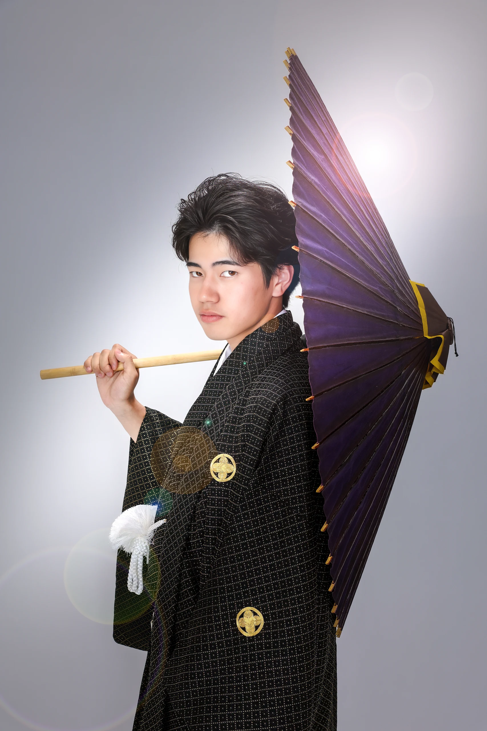 黒金の紋付袴で紫の和傘を肩に掛ける成人男性