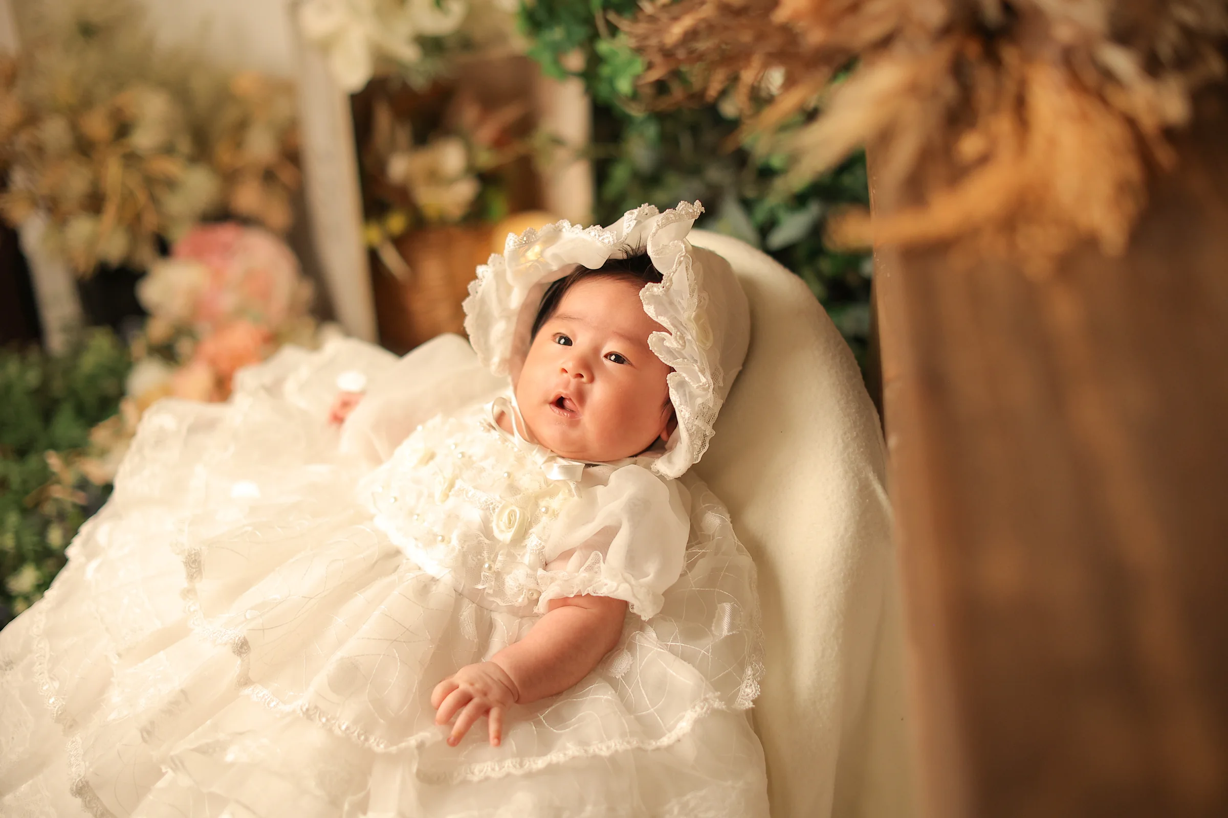 白いベビードレスを着て花に囲まれた赤ちゃん