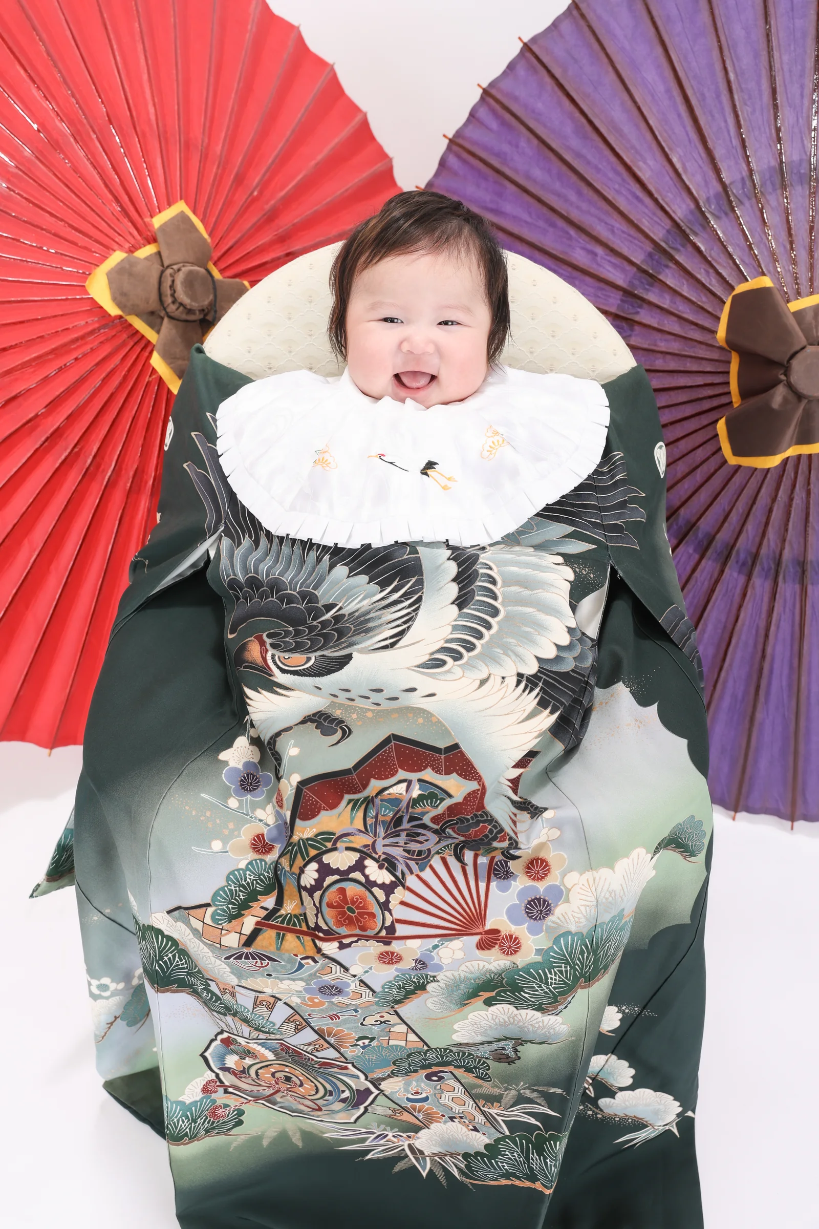 和傘を背景に祝い着をまとって撮影する赤ちゃん
