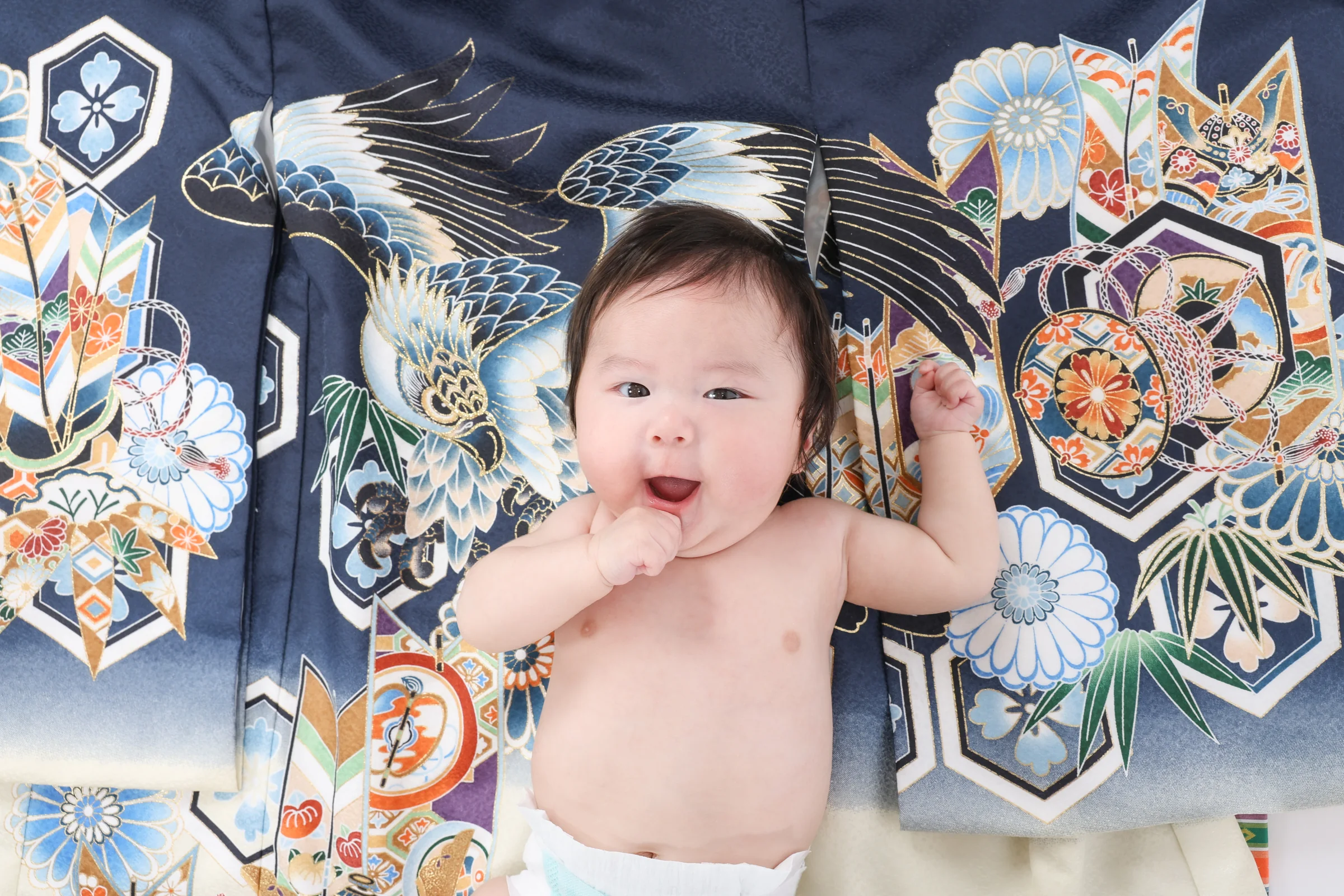 紺の祝い着の上で笑顔を見せる赤ちゃん