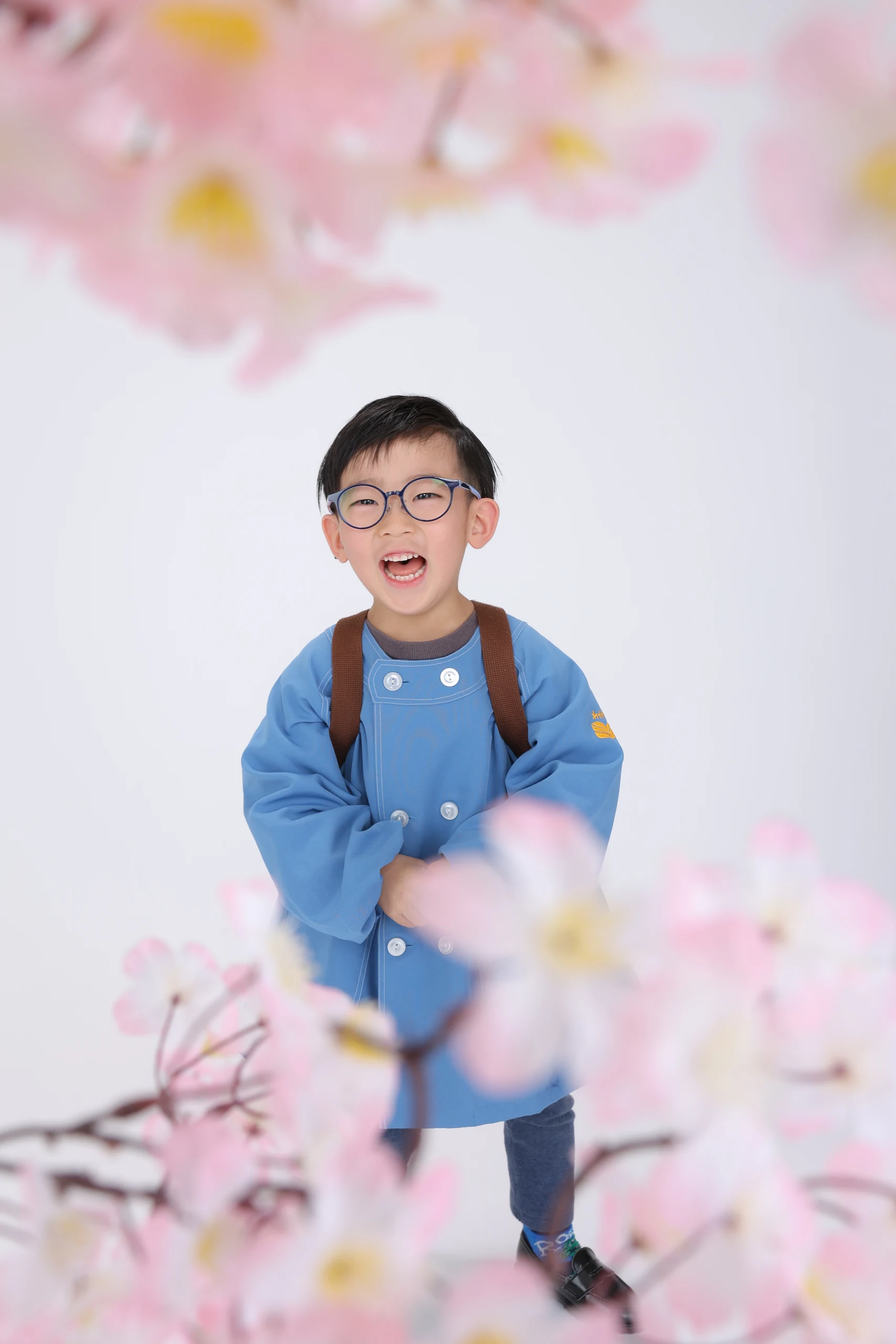 桜の花に囲まれて笑う青い園服とランドセル姿の子ども