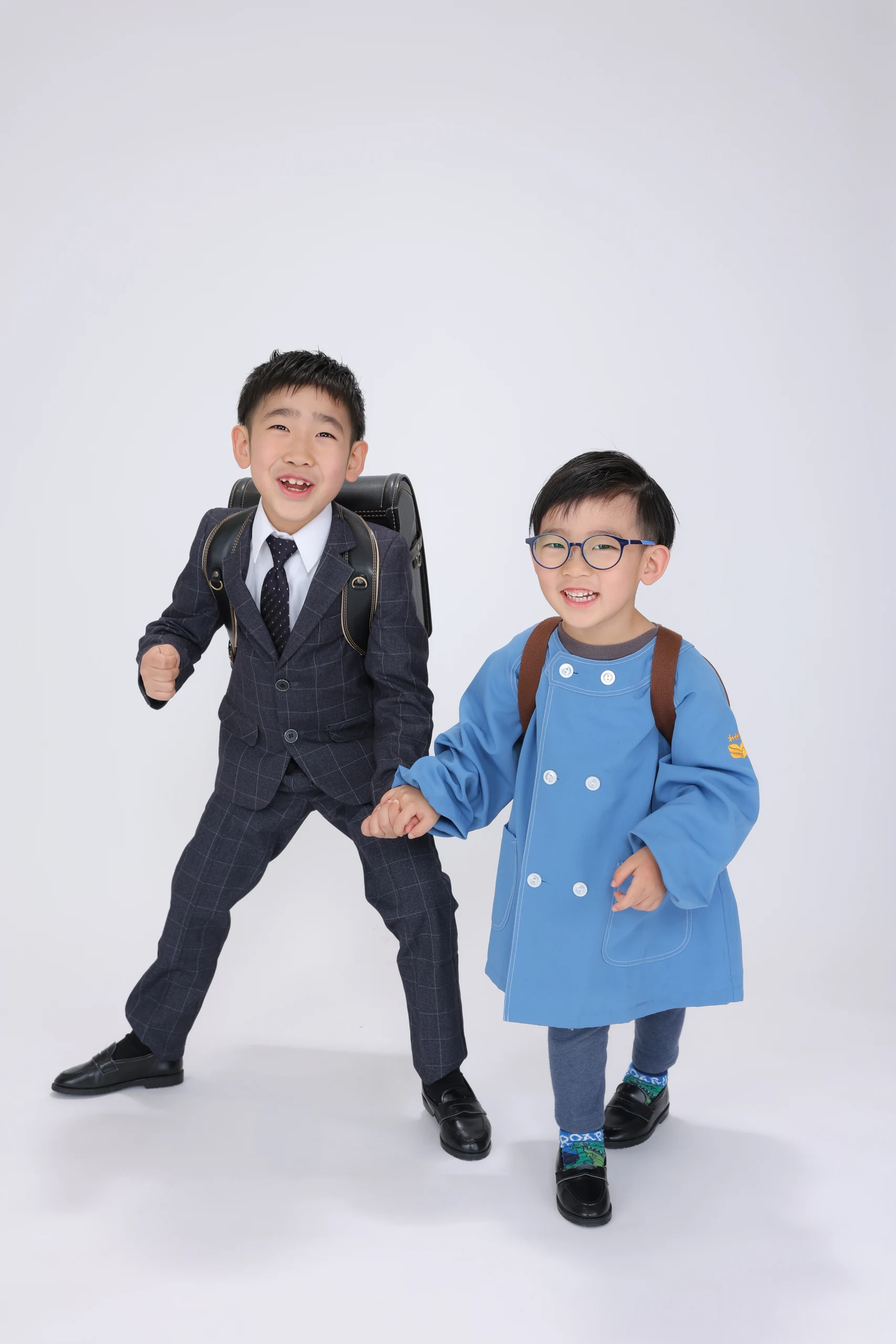 スーツと青い園服で手をつないで走るきょうだい