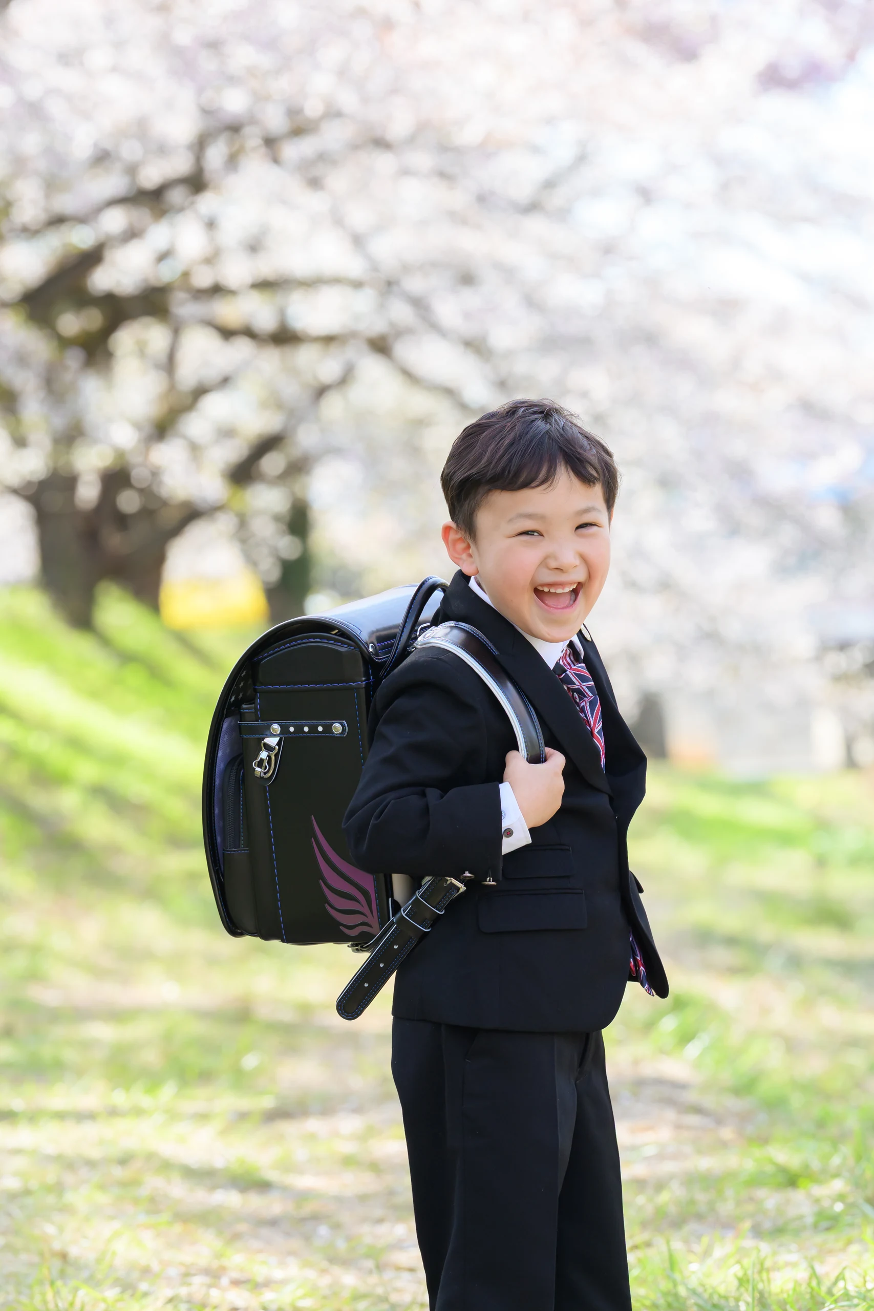満開の桜の下で黒いランドセルを背負って笑う男の子
