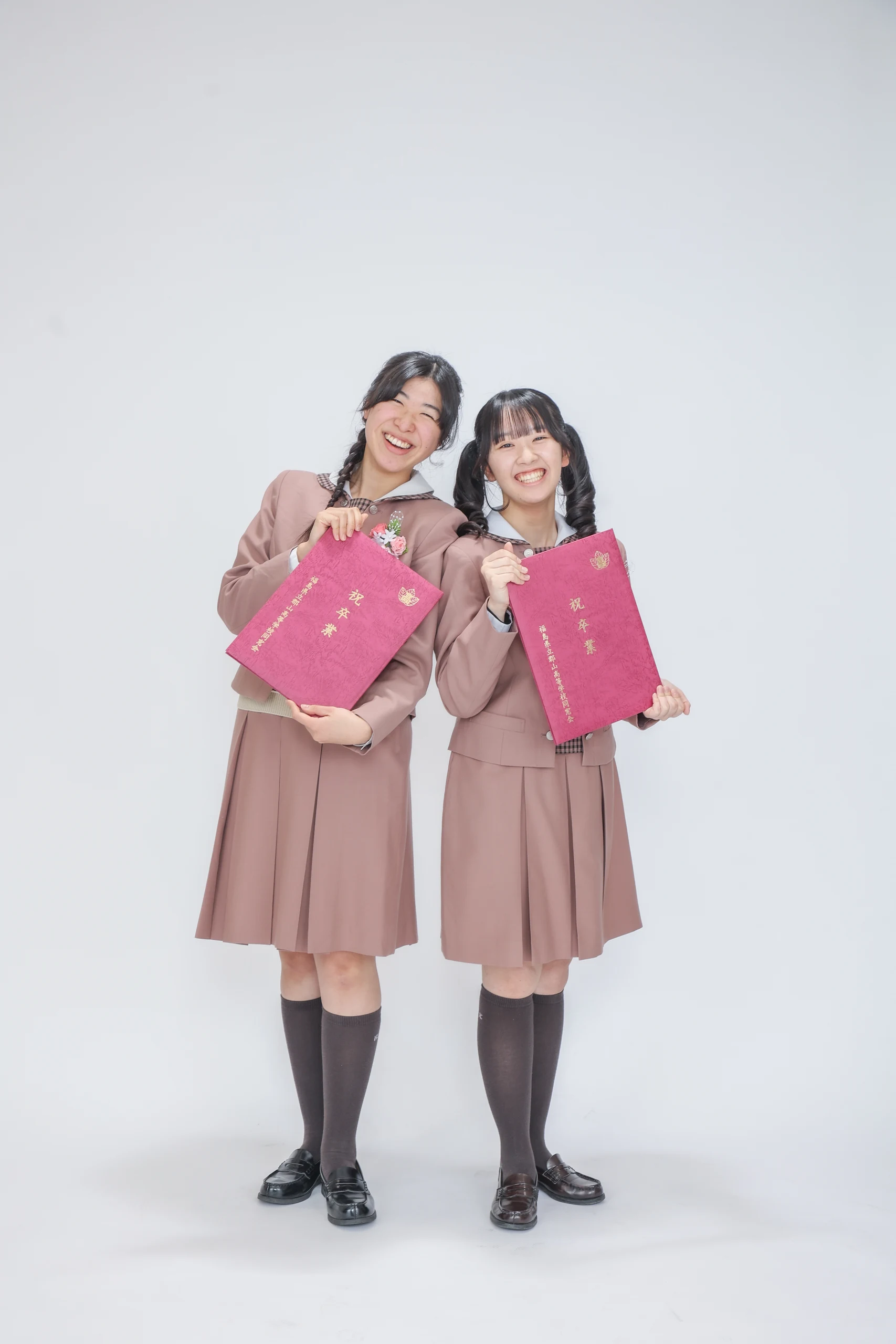 卒業証書を持って並ぶ制服姿の学生二人