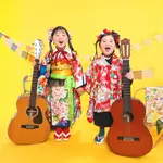 A Shichi-Go-San photo of siblings in traditional Japanese attire smiling side-by-side against a yellow background.