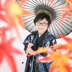 A five-year-old boy smiling with autumn leaves blurred in the foreground and a black Japanese umbrella in the background.