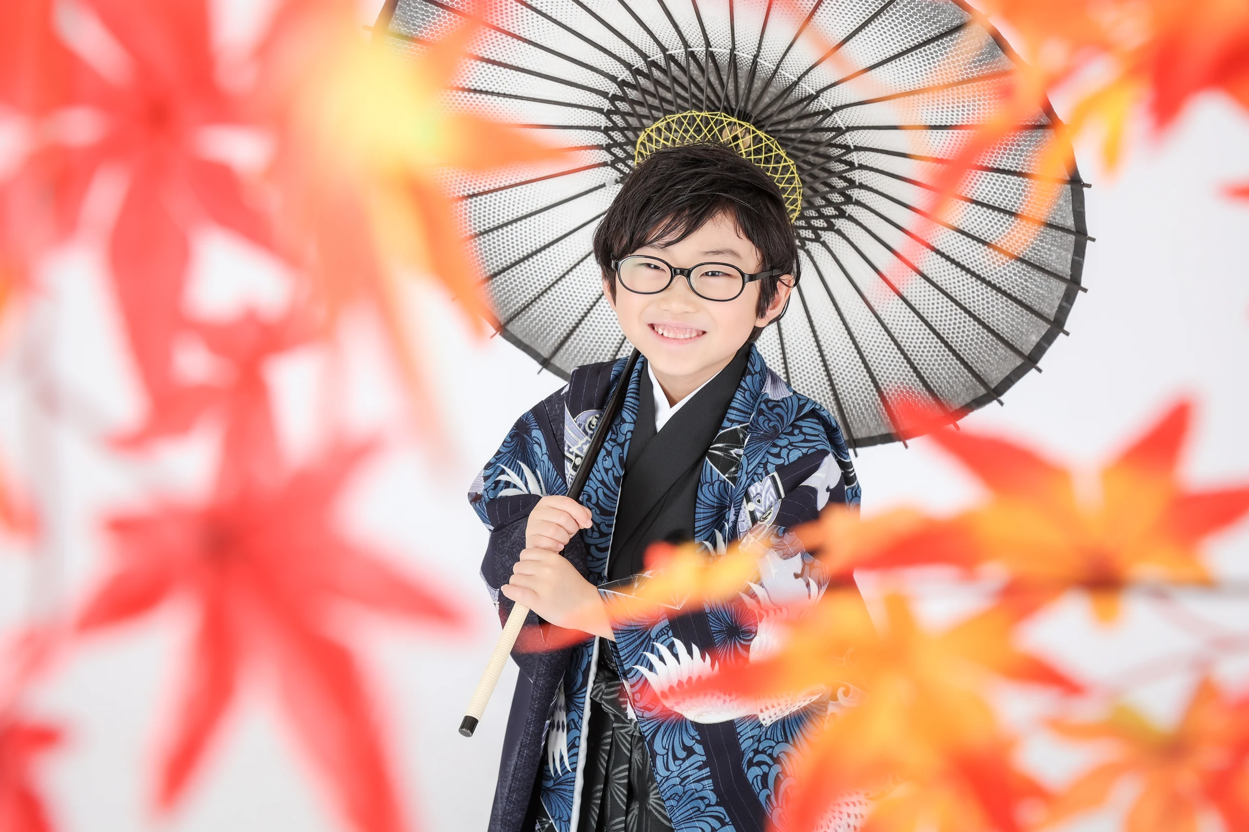 紅葉の前ボケと黒い和傘を背景に笑う五歳の男の子