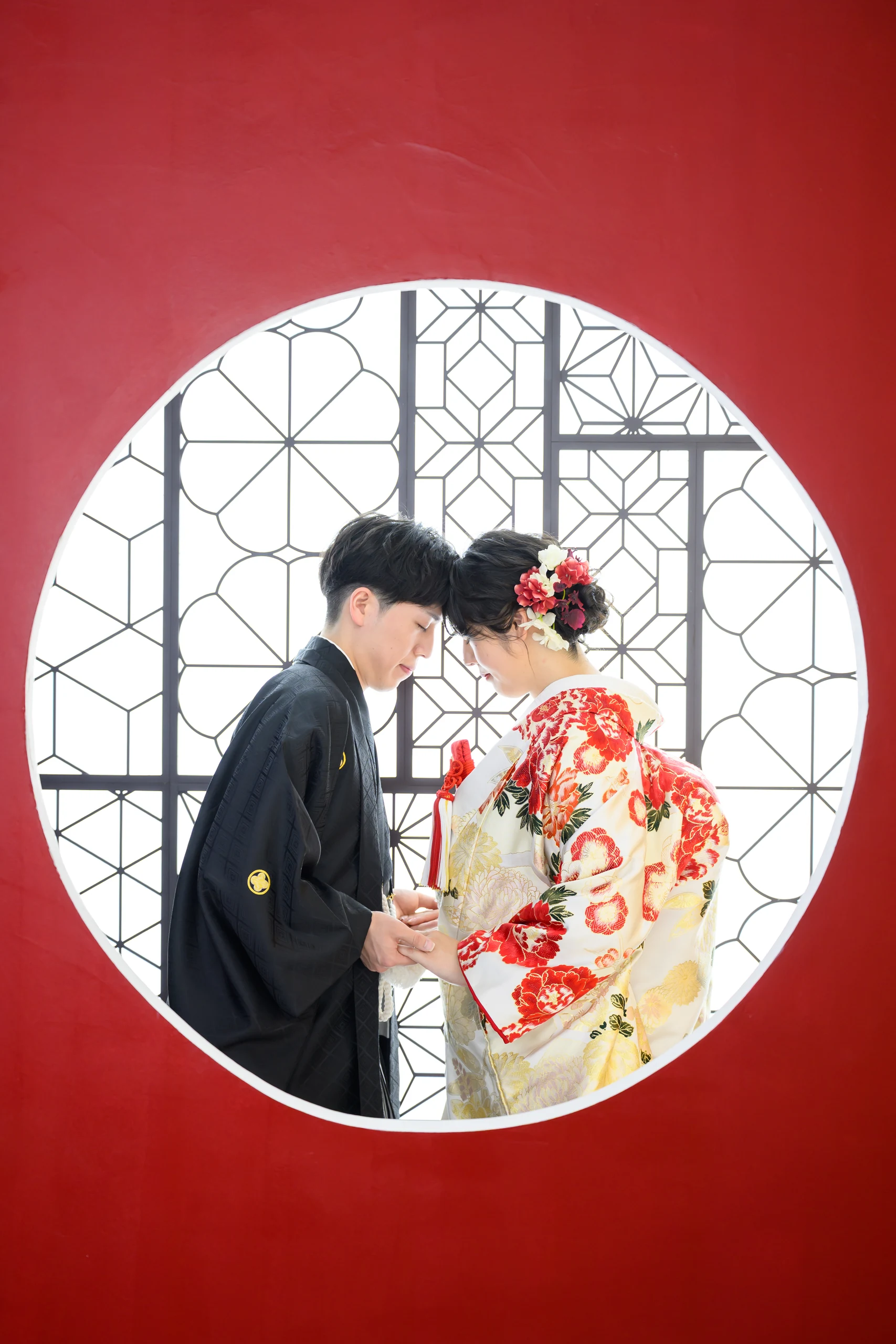 赤い円窓の中で額を寄せ合う色打掛と黒紋付姿の新郎新婦