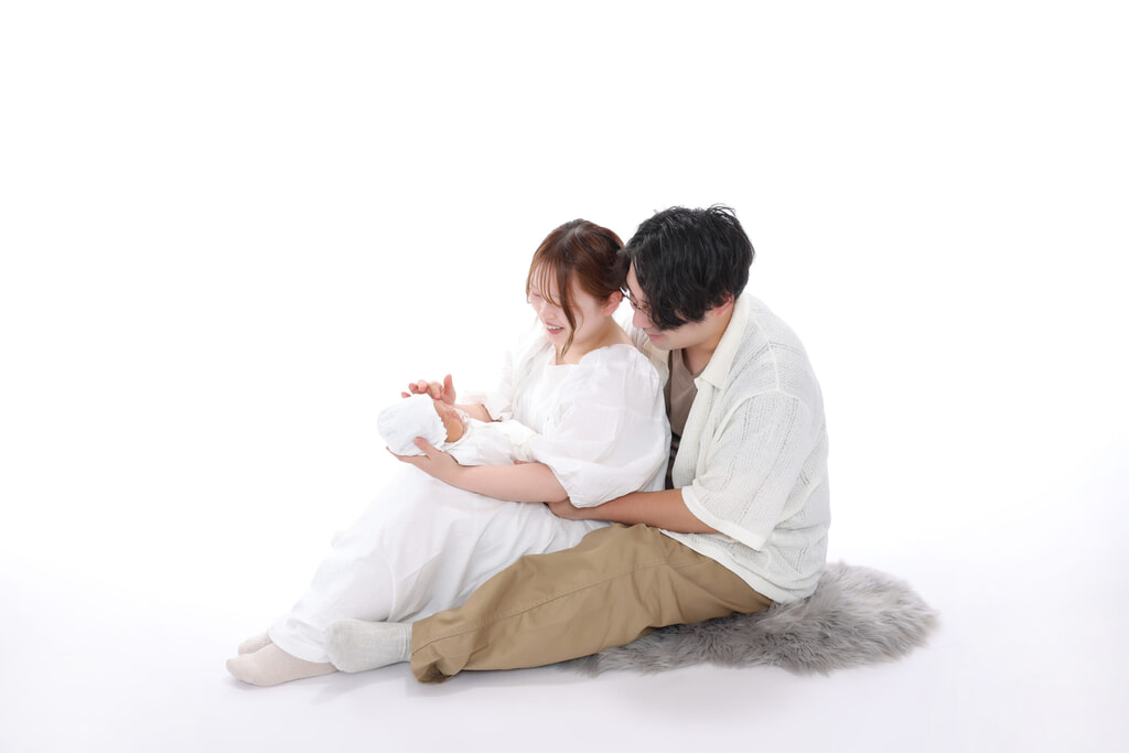白い背景で赤ちゃんを抱き、寄り添うお父さまとお母さま