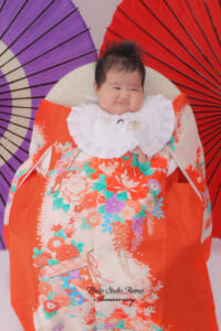 赤い産着を掛けてお宮参り撮影をする赤ちゃん